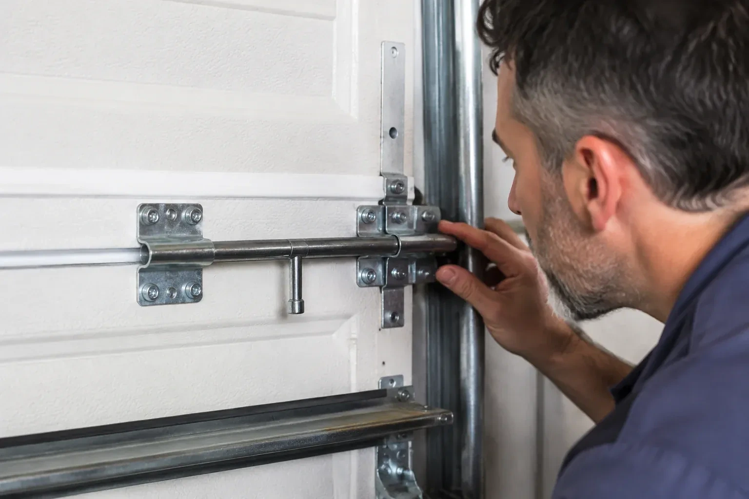 Person leaning close to a white paneled door, one hand on a metal slide-bolt bar mounted across the panel. — Garage Door Manual Lock Repair, Niagara Falls
